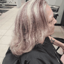 a woman with gray and purple hair is sitting in a chair in a hair salon .