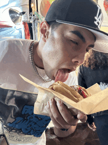 a man wearing a la hat is eating a sandwich with his tongue out