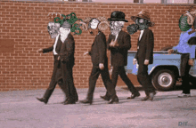 a group of men in suits and gas masks are walking down a street in front of a brick wall