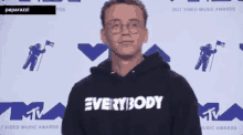 a man wearing a hoodie that says everybody is standing in front of a mtv logo .