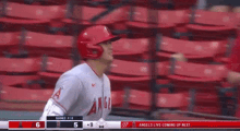 a baseball player wearing a red helmet is standing in front of a row of red seats in a stadium .