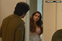 a man looks at a woman in a bra in front of a mirror with a pranay_varma logo above it