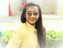 a girl wearing sunglasses and a yellow coat smiles