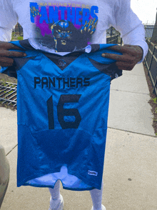 a man holding a blue panthers jersey with the number 16 on it