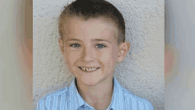 a young boy is smiling for the camera while wearing a blue striped shirt .