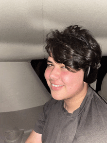 a young man wearing headphones and a grey shirt smiles for the camera