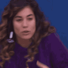 a woman with curly hair wearing a purple sweater and earrings