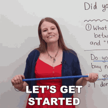 a woman in a red dress is holding a blue stick in front of a whiteboard that says " let 's get started "