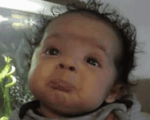 a baby with curly hair is making a funny face and looking at the camera .