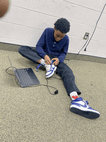 a young boy sits on the floor tying his shoes