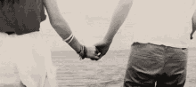 a man and a woman are holding hands in front of a body of water