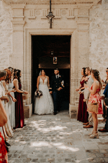 a bride and groom are walking out of a church with their wedding party behind them