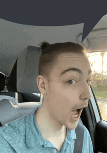 a young man in a blue shirt is sitting in a car with his mouth open