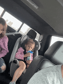 a little girl is sitting in a car seat with a blue bottle