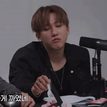a man sitting at a table with a fork in his hand and a microphone in the background