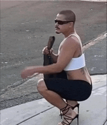 a man squatting down on the sidewalk wearing high heels and a crop top .