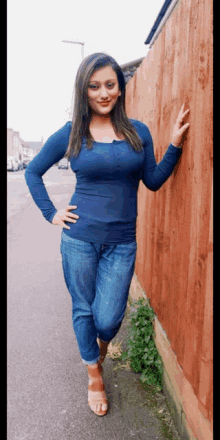 a woman in a blue shirt and jeans is leaning against a red fence