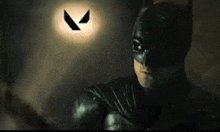 a close up of a man in a batman costume in a dark room with a logo in the background .