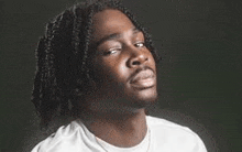 a young man with dreadlocks is wearing a white t-shirt and looking up at the camera .