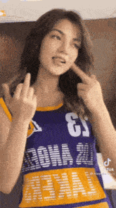 a woman is wearing a purple and yellow jersey and giving the middle finger .