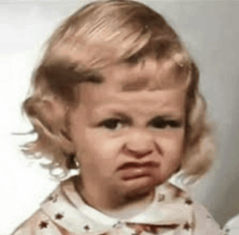 a little girl is making a funny face and looking at the camera .