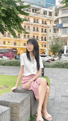 a girl in a white shirt and pink skirt is sitting on a stone wall