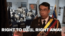 a man in a military uniform is standing in front of a room with people sitting at desks and flags .