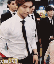 a man in a white shirt and black tie is standing in front of a sign that says exo on it