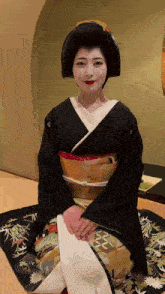 a woman in a black and gold kimono sits on a rug