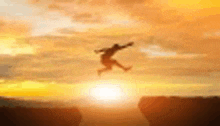 a man is jumping over a cliff at sunset in the air .