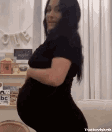 a pregnant woman is sitting on a couch holding her belly and smiling .