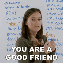 a woman stands in front of a white board with the words " you are a good friend " written on it