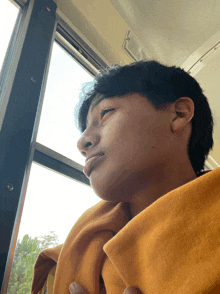 a young man looking out a window with a yellow blanket around his neck