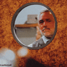 a man with a beard is reflected in a round window with trashtvtroll written on the bottom