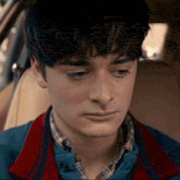 a close up of a young man 's face with a blue shirt and red collar