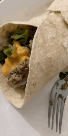 a close up of a tortilla with meat and cheese with a fork next to it