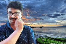 a man with glasses and a mustache is standing in front of a body of water