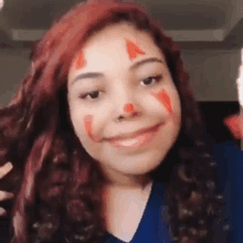 a woman with red hair and a clown makeup on her face is smiling .