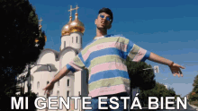 a man in a striped shirt is standing in front of a church with the words " mi gente esta bien " on the bottom