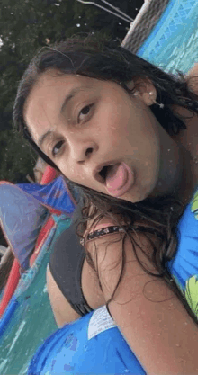 a young girl is sticking her tongue out in a pool while wearing a life preserver .