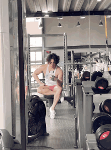 a man taking a picture of himself in a gym with a fan and dumbbells with the number 15 on them