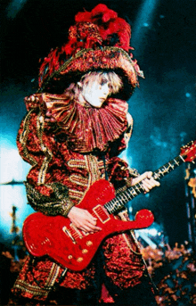 a man in a red and gold outfit is holding a red guitar