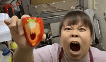 a woman is holding a red pepper with a hole in it and making a funny face .