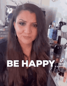 a woman is standing in front of a shelf with a bottle of wine and a sign that says be happy .