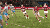 a group of men are playing a game of rugby on a field with an advert for univeral of salford in the background