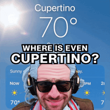 a man wearing sunglasses and headphones stands in front of a screen that says cupertino