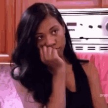 a woman with long black hair is sitting in front of a stove in a kitchen .