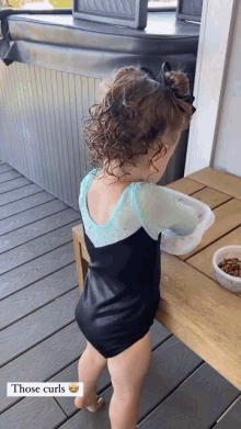 a little girl in a black leotard is standing on a deck next to a bowl of food and a hot tub .