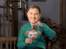 a man wearing a green sweater with a clown on it is smiling