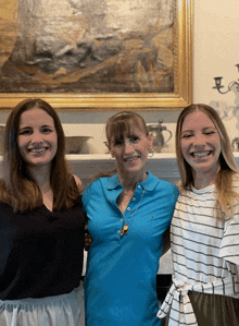 three women posing for a picture in front of a framed painting